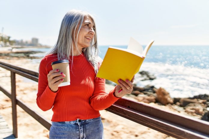 Middle,Age,Grey-haired,Woman,Drinking,Coffee,And,Reading,Book,At
