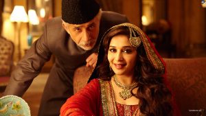 Bride in a red and gold traditional outfit with ornate jewelry, smiling as an older man leans in beside her in a warm, dimly lit room.