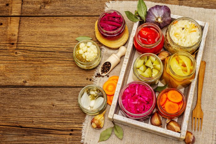 The Best Foods for Your Gut During the Monsoon Assorted pickled vegetables in glass jars on a rustic wooden table with a wooden crate and fork nearby