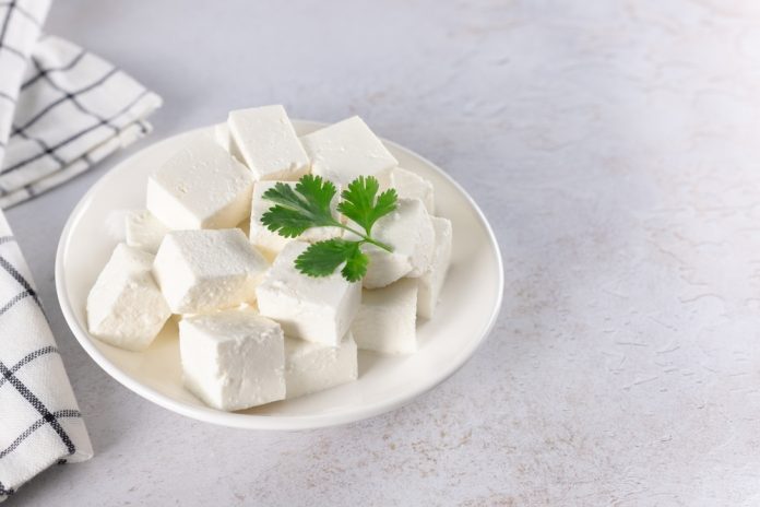 Traditional,Indian,Paneer,Cheese,Slices,Cubes,On,White,Background.,Copy Plate of cubed white cheese with a parsley sprig on top.